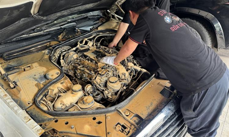 Một người thợ máy giàu kinh nghiệm đang dùng đèn pin kiểm tra kỹ lưỡng phần khung gầm và động cơ của một chiếc xe tải 10 tấn đã qua sử dụng.