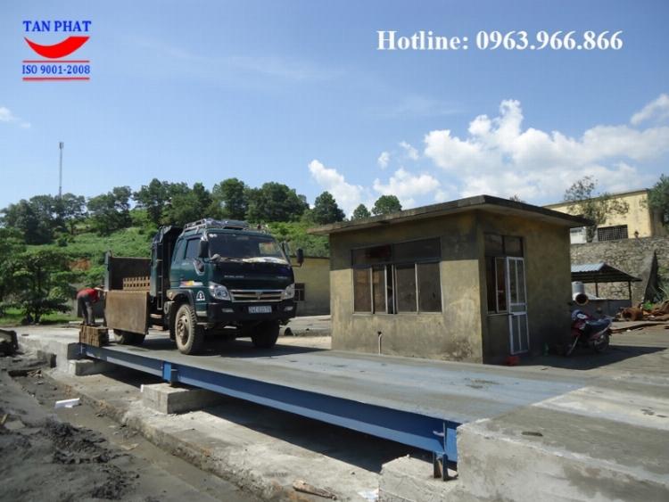 Một trạm cân xe tải điện tử hiện đại kiểu nổi với một chiếc xe container đang từ từ di chuyển lên bàn cân để xác định tải trọng.